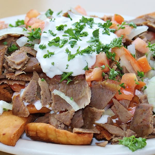 A close-up of a Greek gyro plate with meat, tomatoes, onions, and tzatziki sauce.