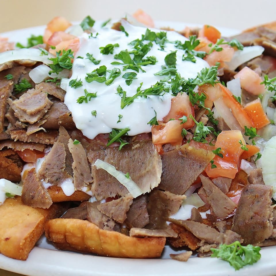 A close-up of a Greek gyro plate with meat, tomatoes, onions, and tzatziki sauce.
