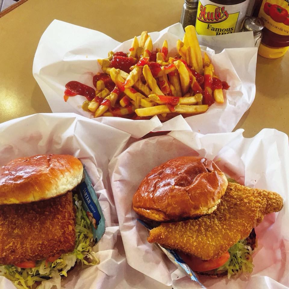 Two Hub's fish sandwiches with lettuce and tomato, alongside a basket of french fries with ketchup.