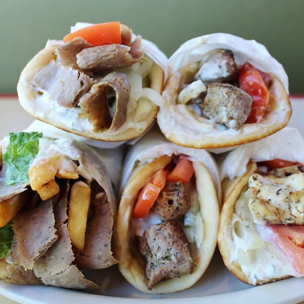A close-up of several Hub's Restaurant Greek gyros, some with fries, on a white plate.